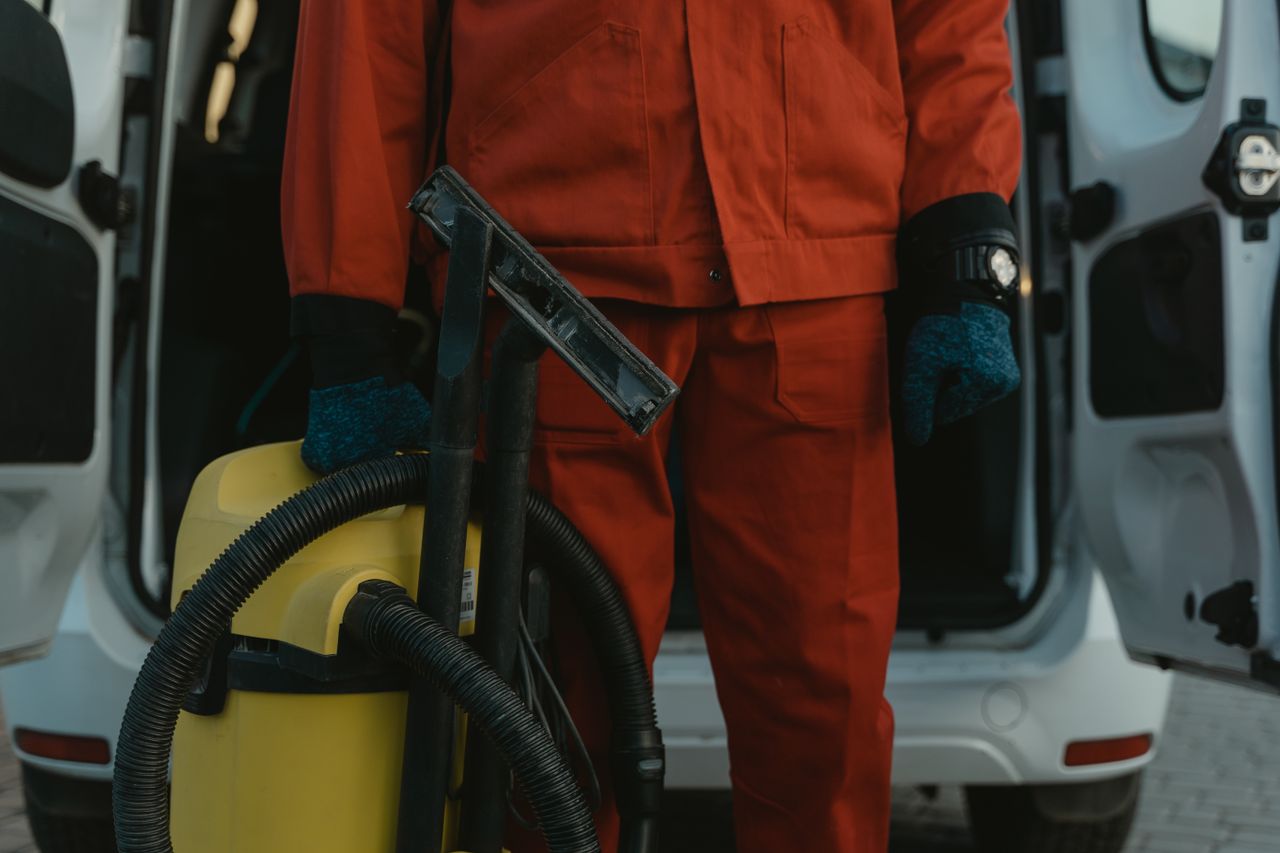 journey A professional cleaner in a red uniform holding a vacuum near a van, ready for service.